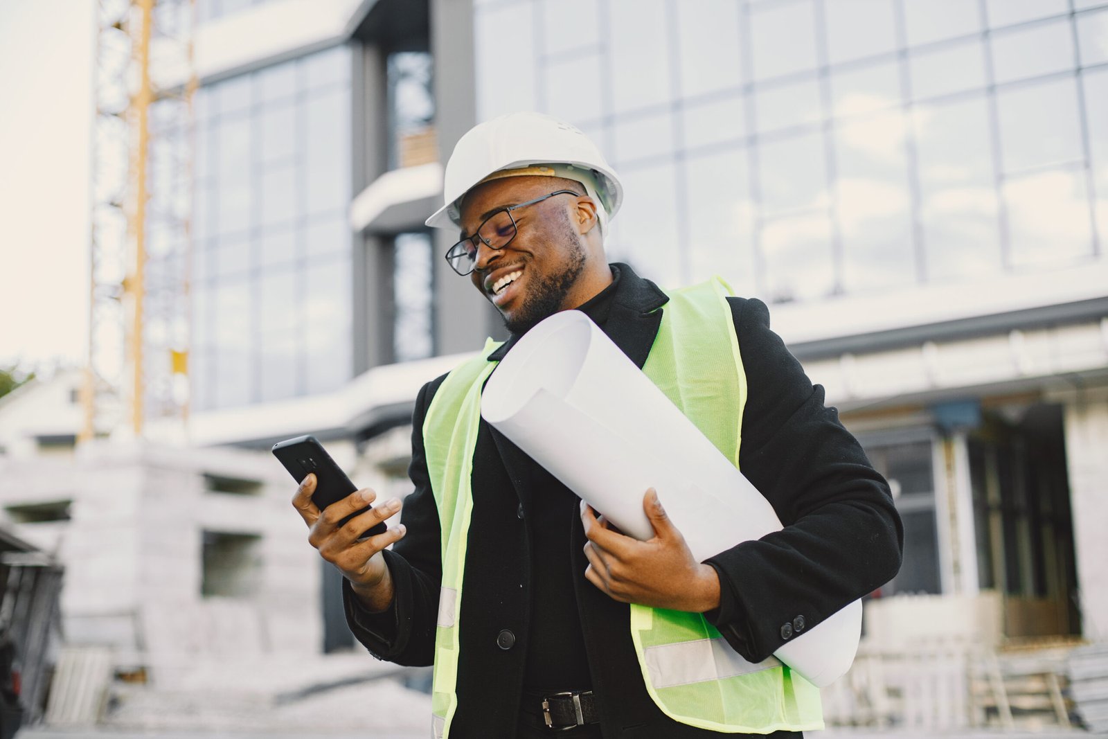 Young black race man with blueprint stading near glass building. Talking by phone.